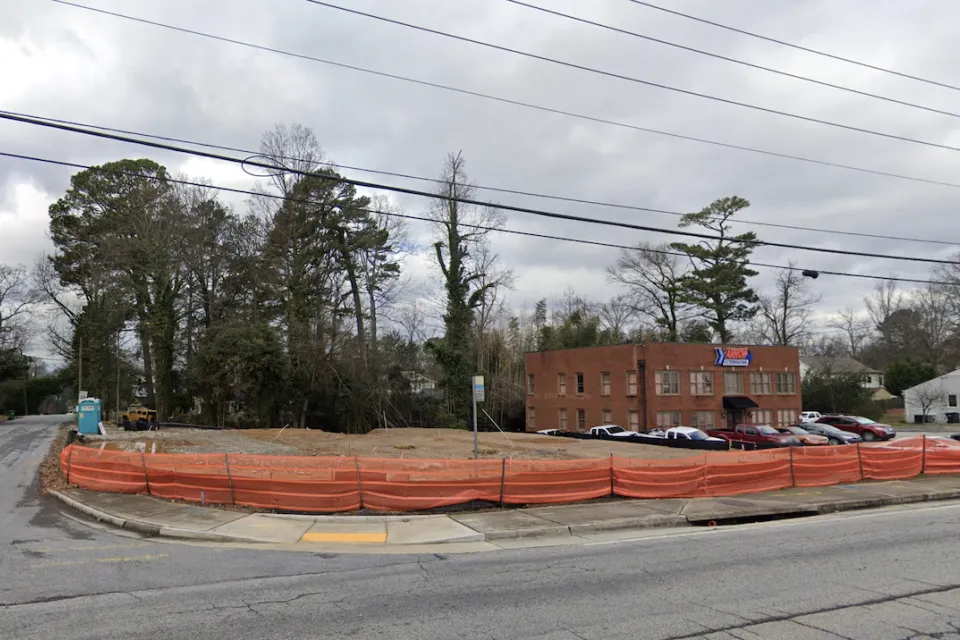 Vacant corner lot in Atlanta, Georgia surrounded with low orange plastic construction fencing.